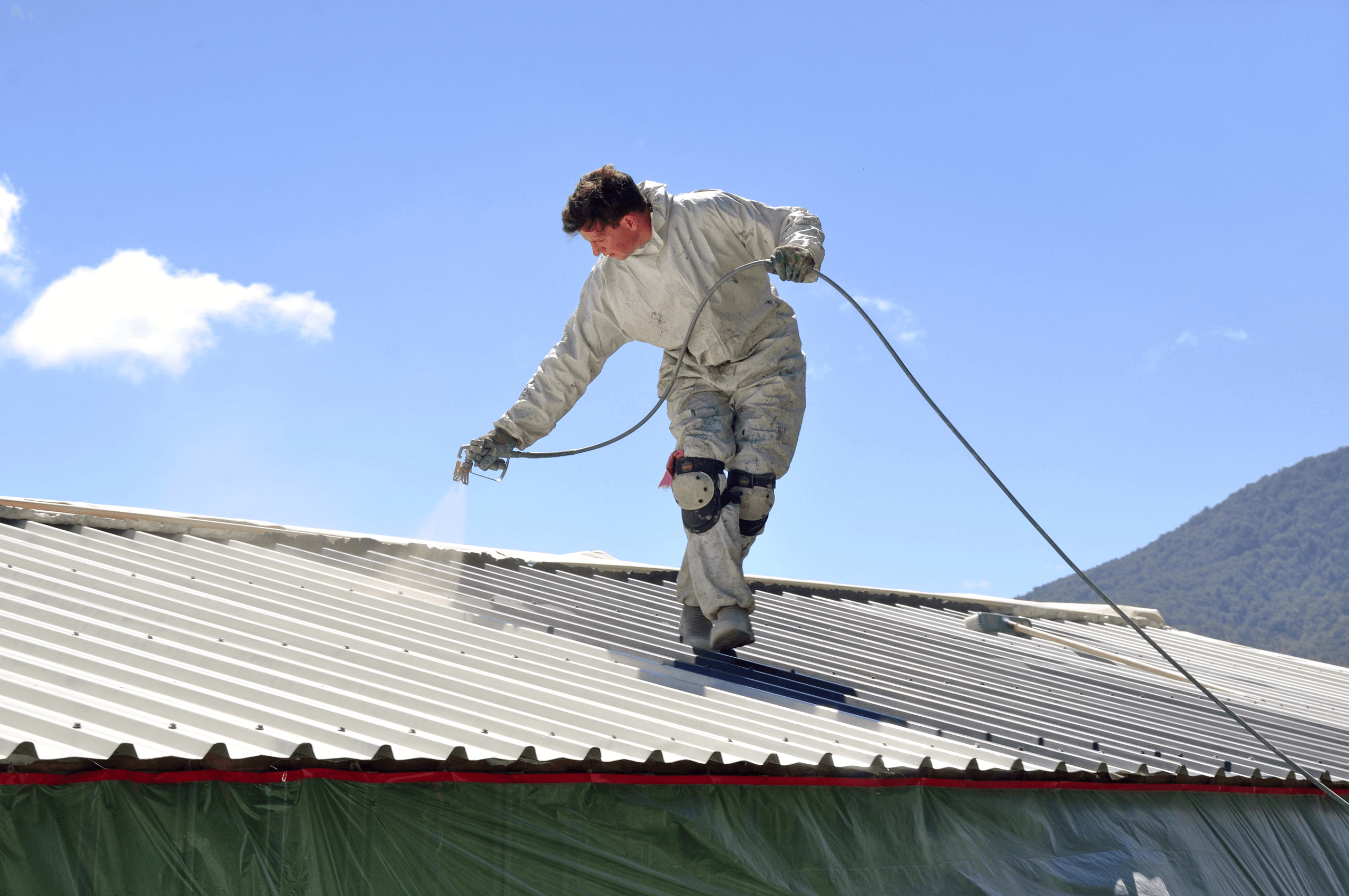 Worker spraying coating on metal roof