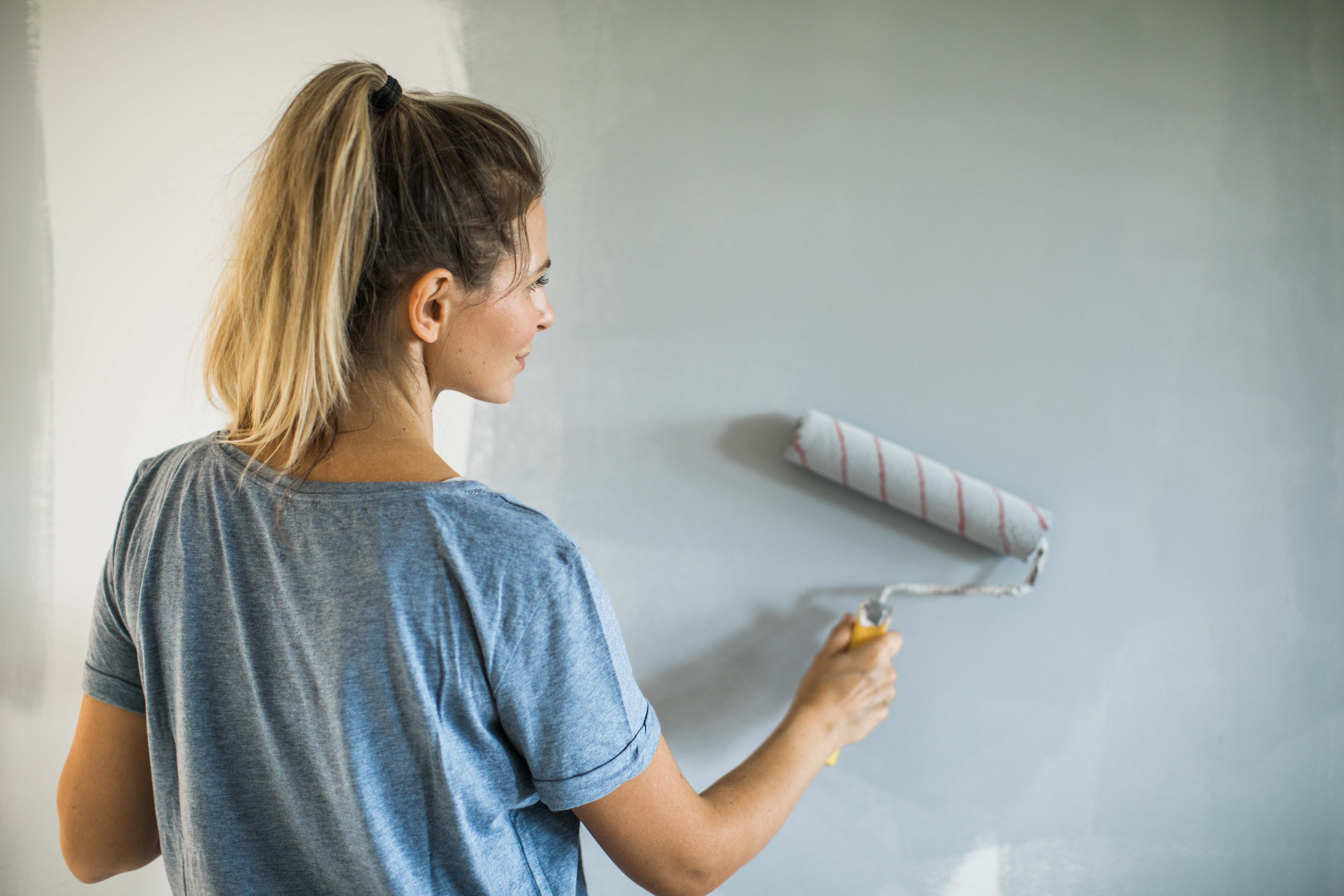 woman rolling gray/blue paint on wall